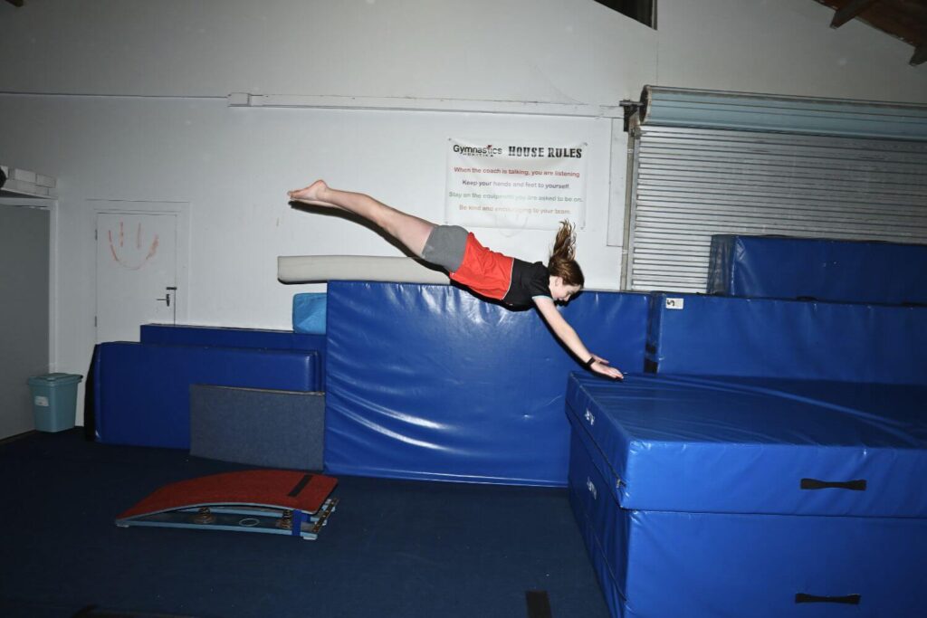 Person in mid-air performing a front flip onto a blue mat in a gymnastics facility.