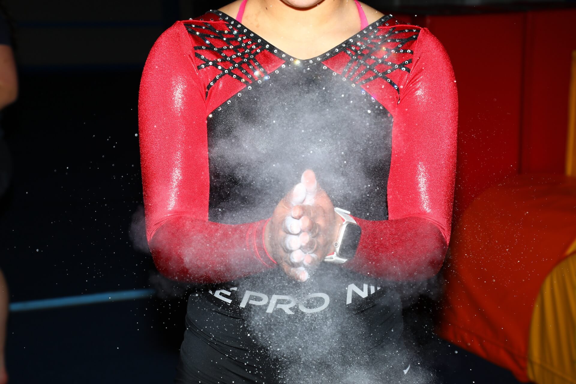 A person in a red and black athletic outfit claps their hands, creating a cloud of chalk dust.